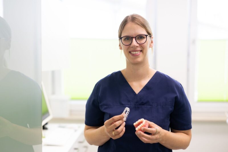 Zahnärztin hält eine transparente Invisalign-Schiene und ein Zahnmodell – Invisalign beim Zahnarzt in Lünen